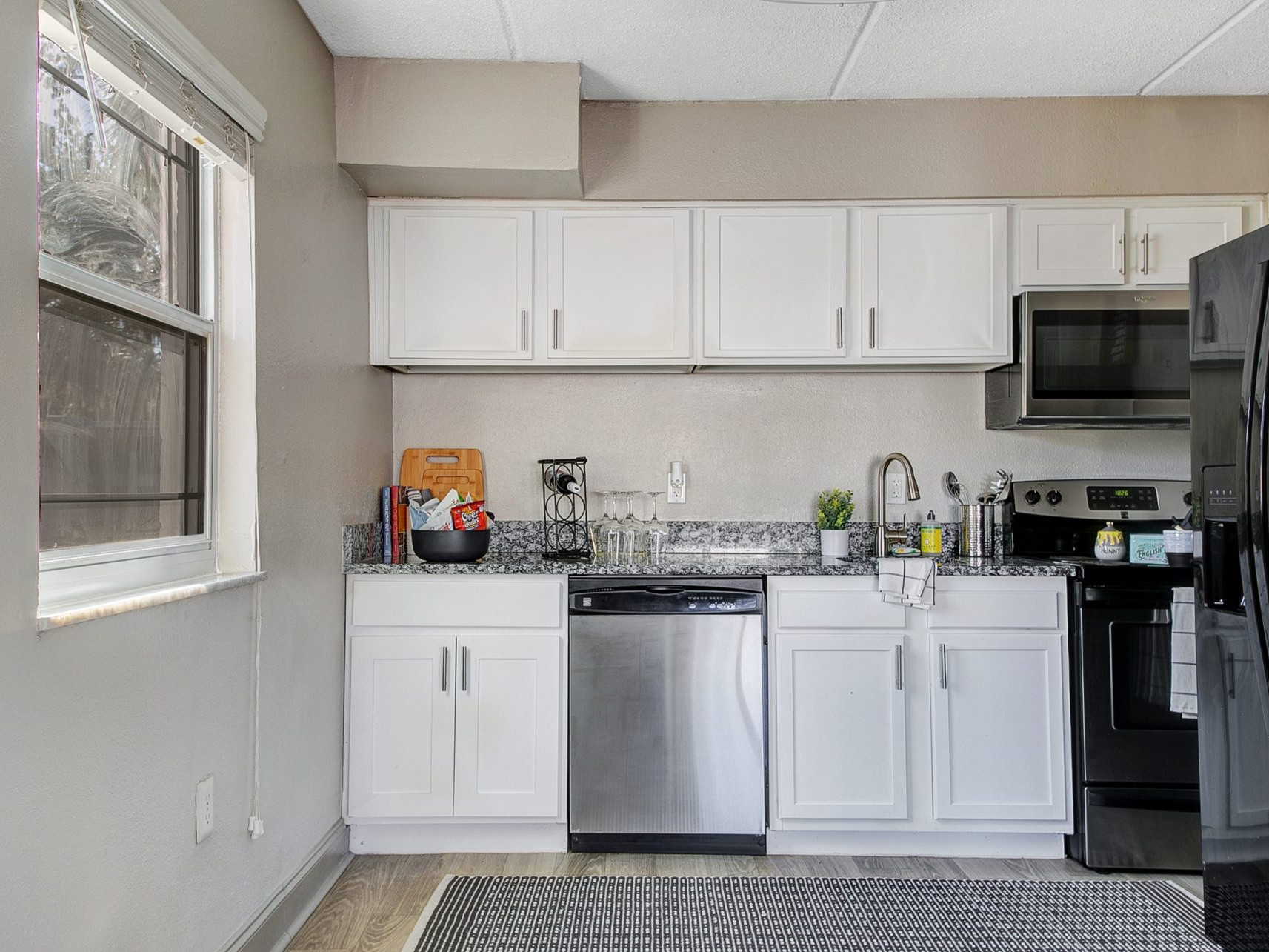 A kitchen with white cabinets, stainless steel appliances, and a window.