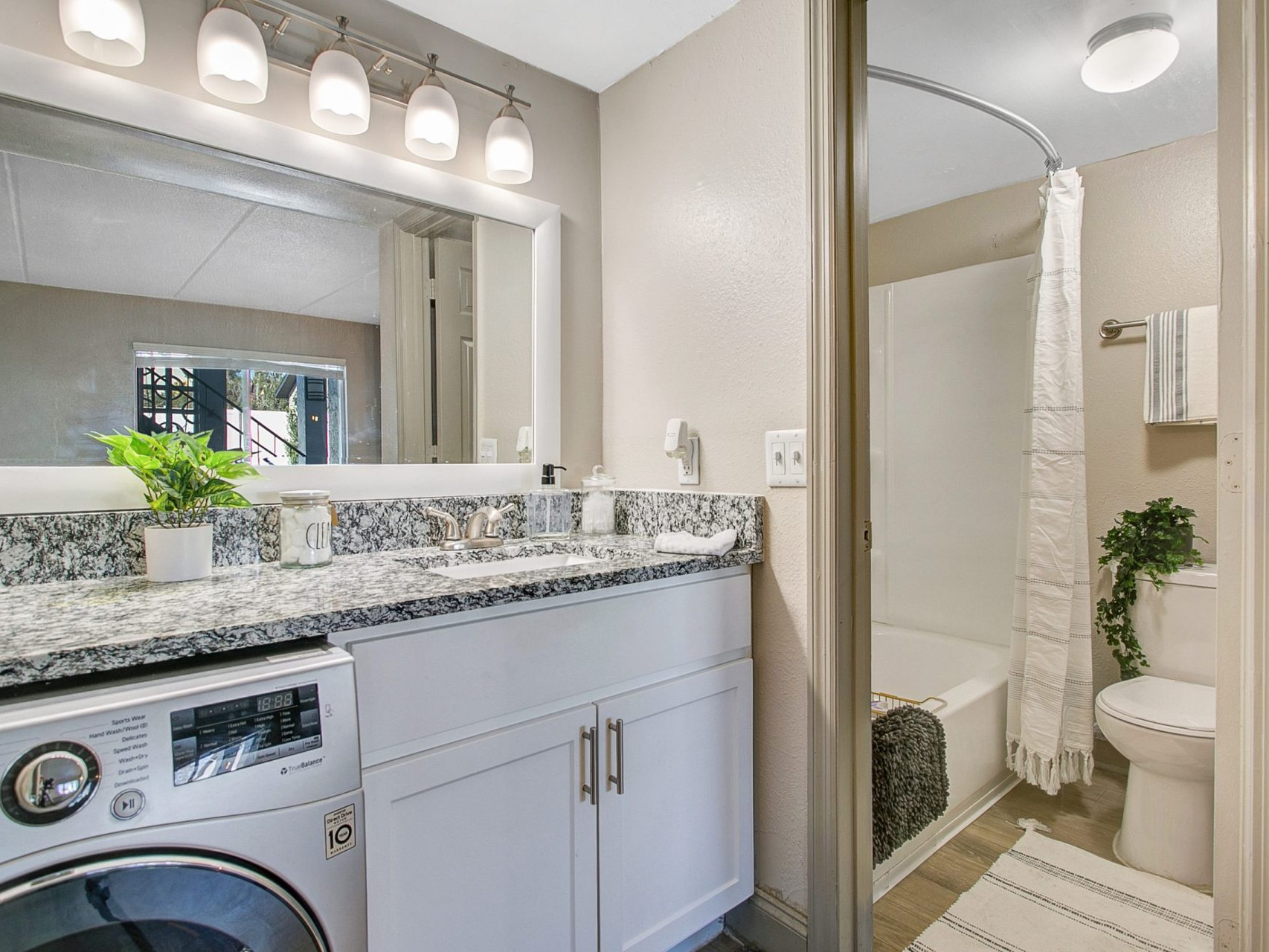 A bathroom with a large counter and mirror, under-the-sink washer and dryer, and sliding door with access to the shower/tub and toilet.