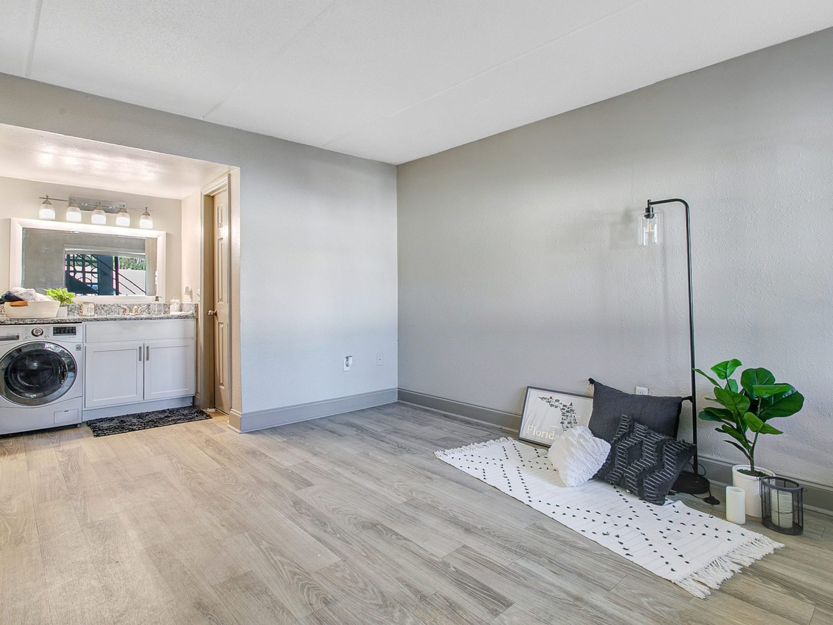 A living room with open access to a laundry area with a washer/dryer, built-in counters, and a large mirror.