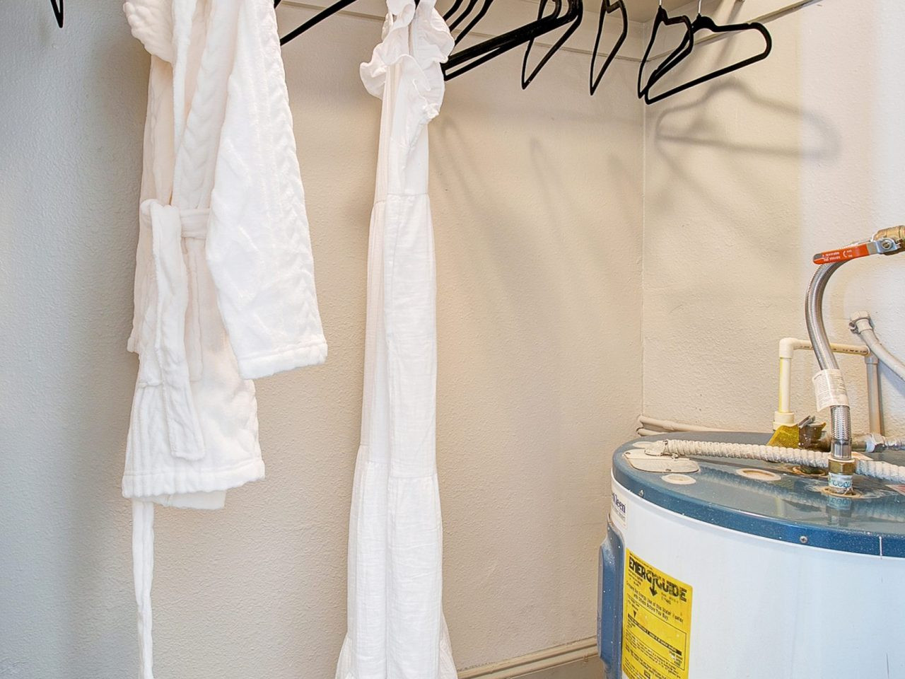 A walk-in closet with clothes hanging inside near a water heater unit.
