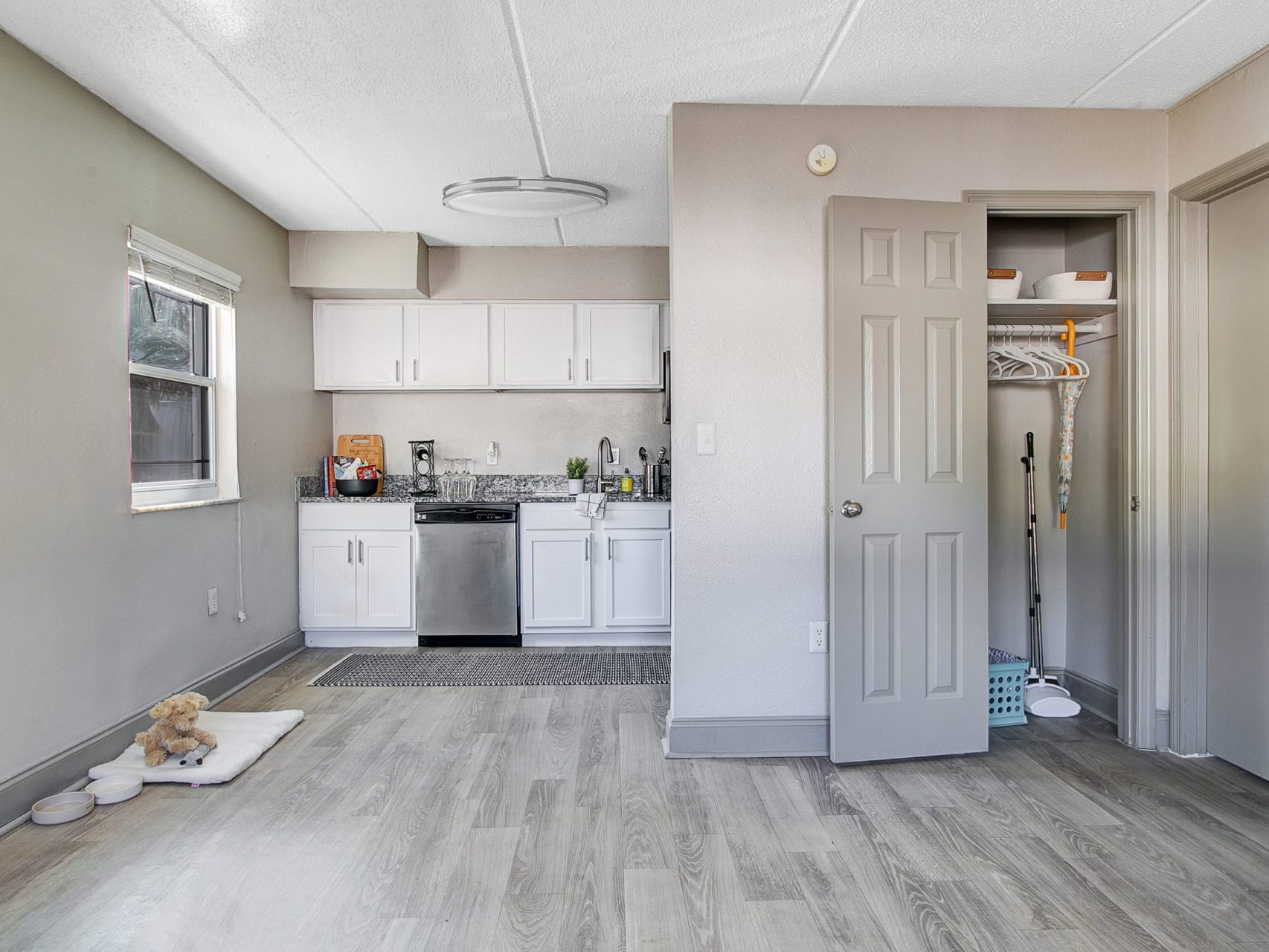 A living room with access to a kitchen near a window and a linen closet.