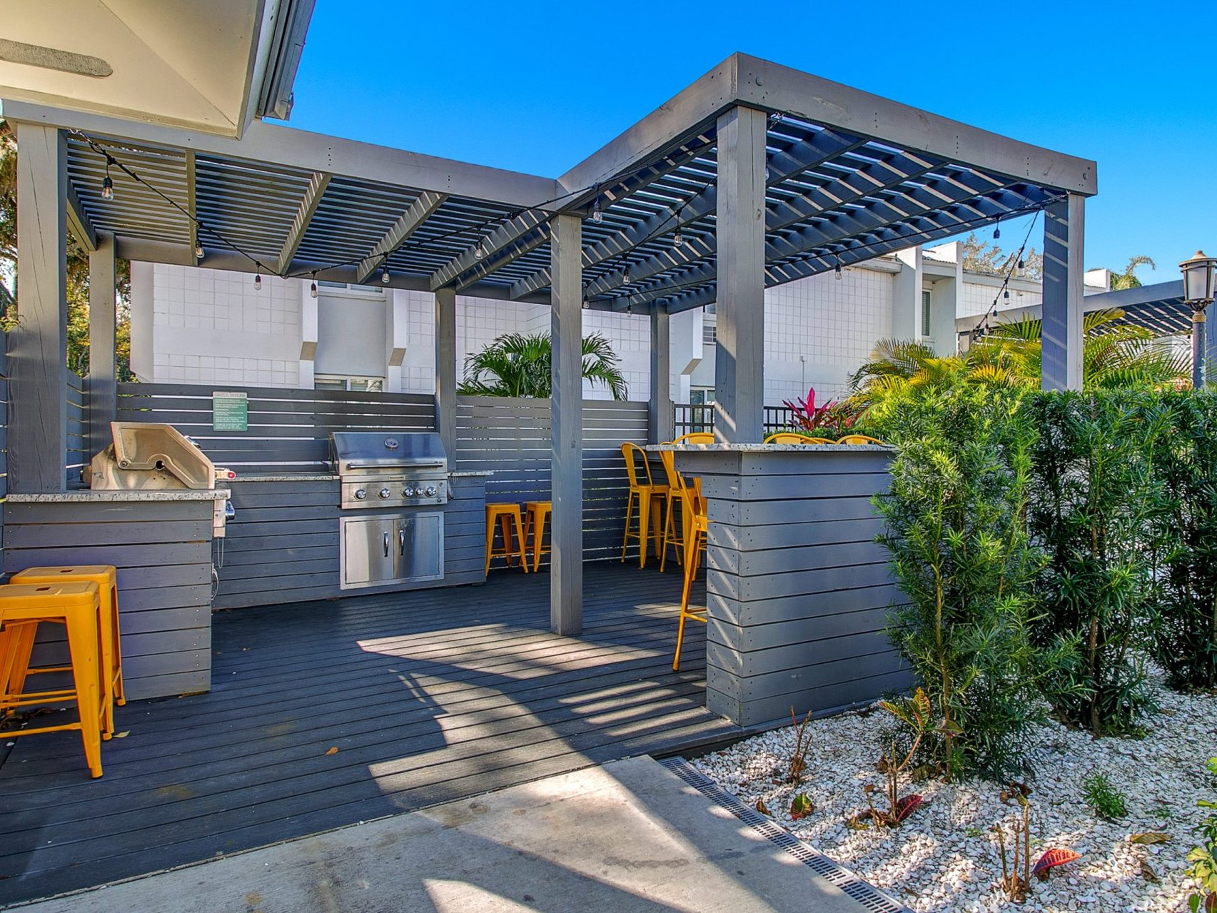 Outdoor community area with outdoor bar seating, barbecue grills, and pergola shelters with string lights.